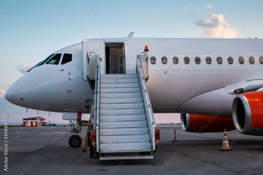 Obraz premium Modern passenger airplane with boarding stairs at the airport apron