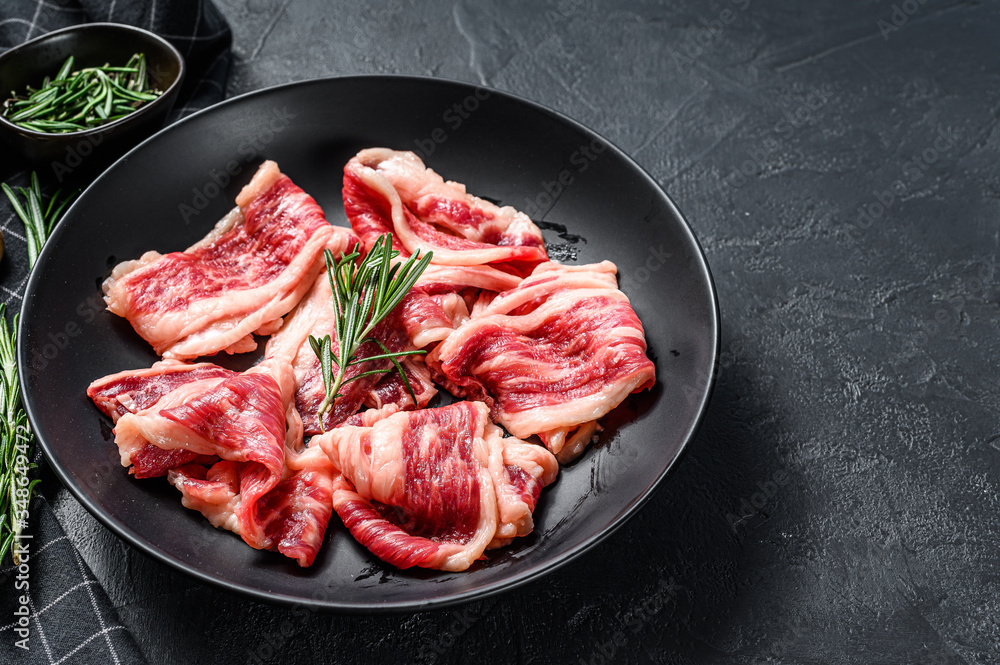 Raw beef bacon, marbled meat in a plate. Black background. Top view. Copy space