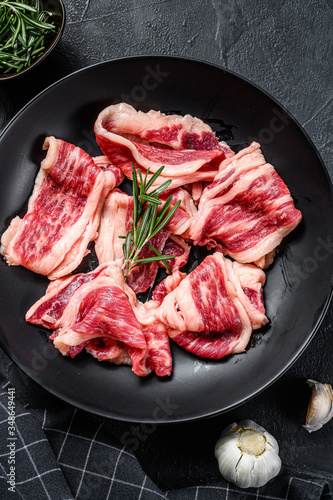 Raw beef bacon, marbled meat in a plate. Black background. Top view