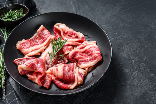 Raw beef bacon, marbled meat in a plate. Black background. Top view. Copy space