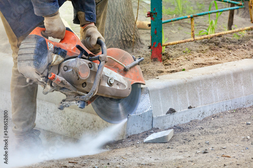 Worker at a construction site using a concrete saw cuts concrete curbs.