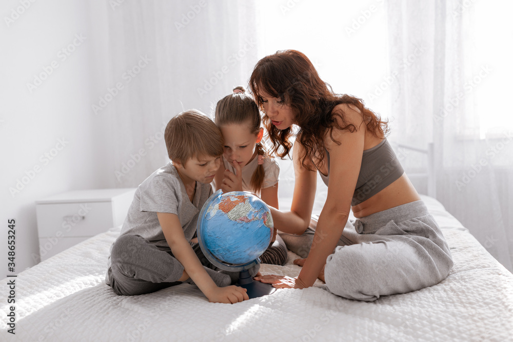 Happy family mother, daughter and son are playing with a terrestrial globe at home in bedroom. Stay home concept. Happy family mother, daughter and son are playing with a terrestrial globe at home in bedroom. Stay home concept.