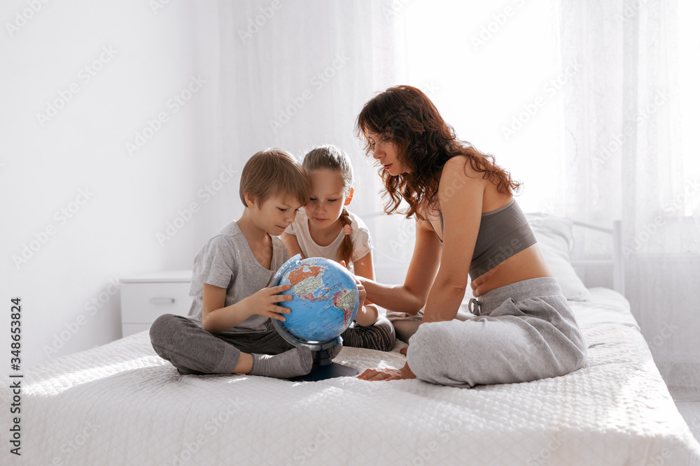 Happy family mother, daughter and son are playing with a terrestrial globe at home in bedroom. Stay home and homeconcept. Happy family mother, daughter and son are playing with a terrestrial globe at home in bedroom. Stay home and homeconcept.