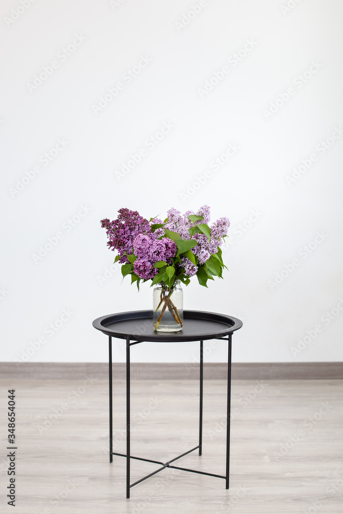 Fototapeta premium Bouquet of beautiful spring lilac flowers in vase on black vintage coffee table, rustic home decor. Bouquet of lilac flowers on an isolated white background. Interior Design. Space for text. Scandi 