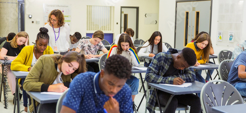 High school teacher supervising students taking exam at desks photo