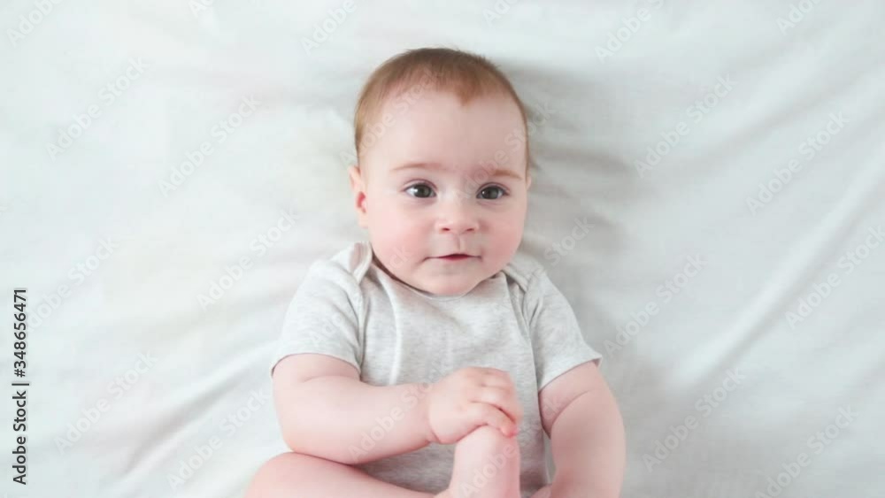 Little baby girl playing with her legs on white bed. Top view Little baby girl playing with her legs on white bed. Top view