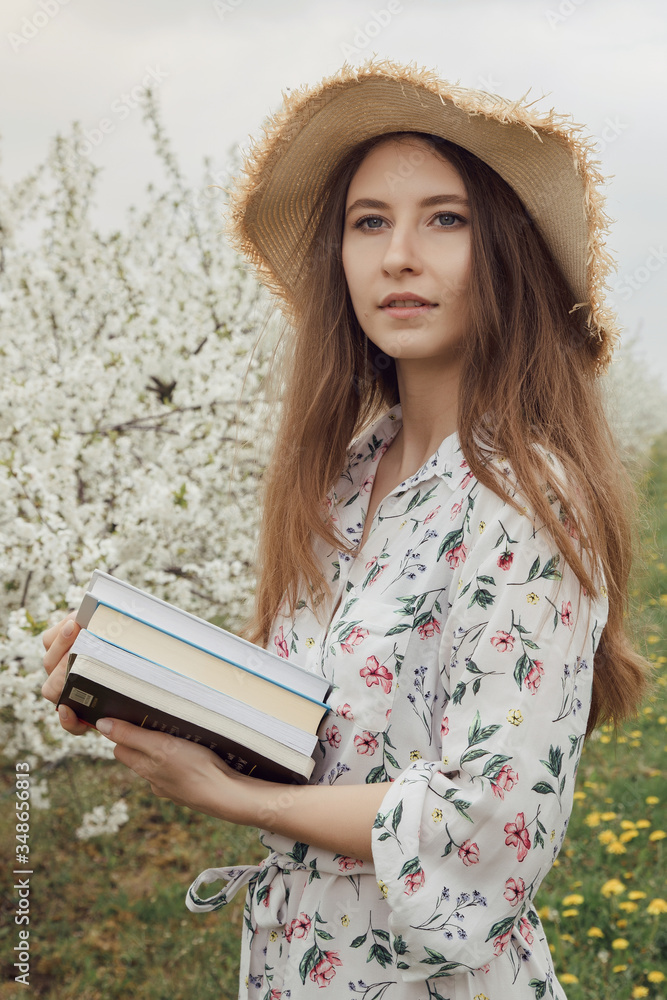 Girl reading a book in the spring garden. Gorgeous woman in hat and dress on nature. Camping with a book.