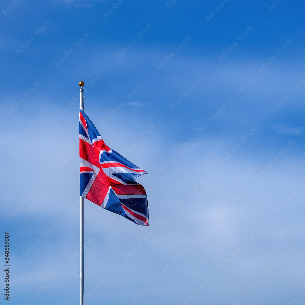 Great Britain Union Jack flag flying on a flagpole in breeze with blue sky and copy space.
