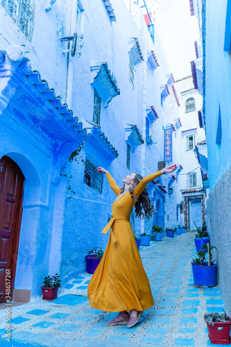 A beautiful caucasian woman in a yellow dress is dancing in a street in a blue city in Morocco. Chefchaouen. © viktoriia1974