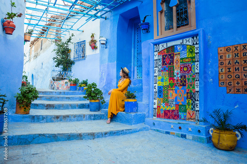 Beautiful caucasian woman in a yellow dress and a boater hat posing in a blue city in Morocco. Chefchaouen. © viktoriia1974