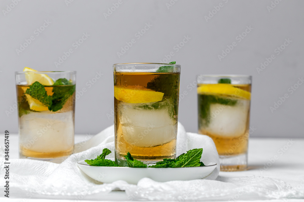 Fototapeta premium tea with ice, mint and lemon wedges on white table