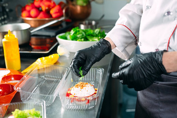 Food delivery in the restaurant. The chef prepares food in the restaurant and packs it in disposable dishes.