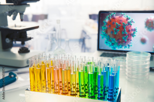 Multicolor vials on laboratory table next to coronavirus on screen photo