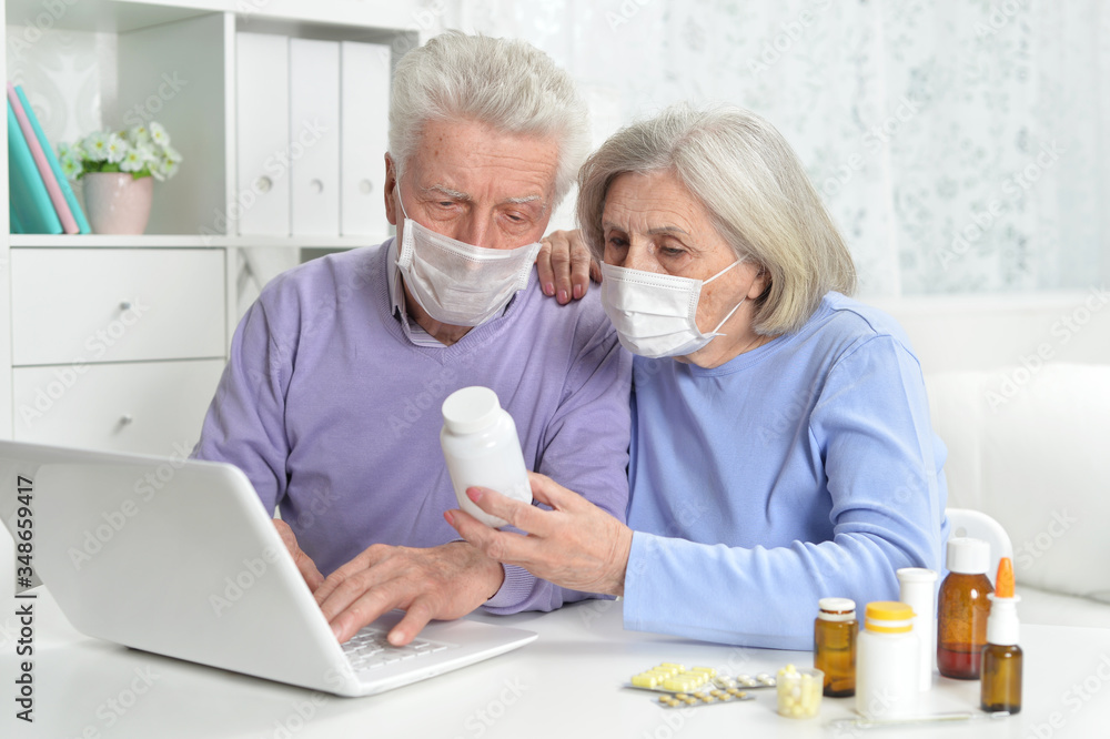 Fototapeta premium Ill senior couple with facial masks using laptop
