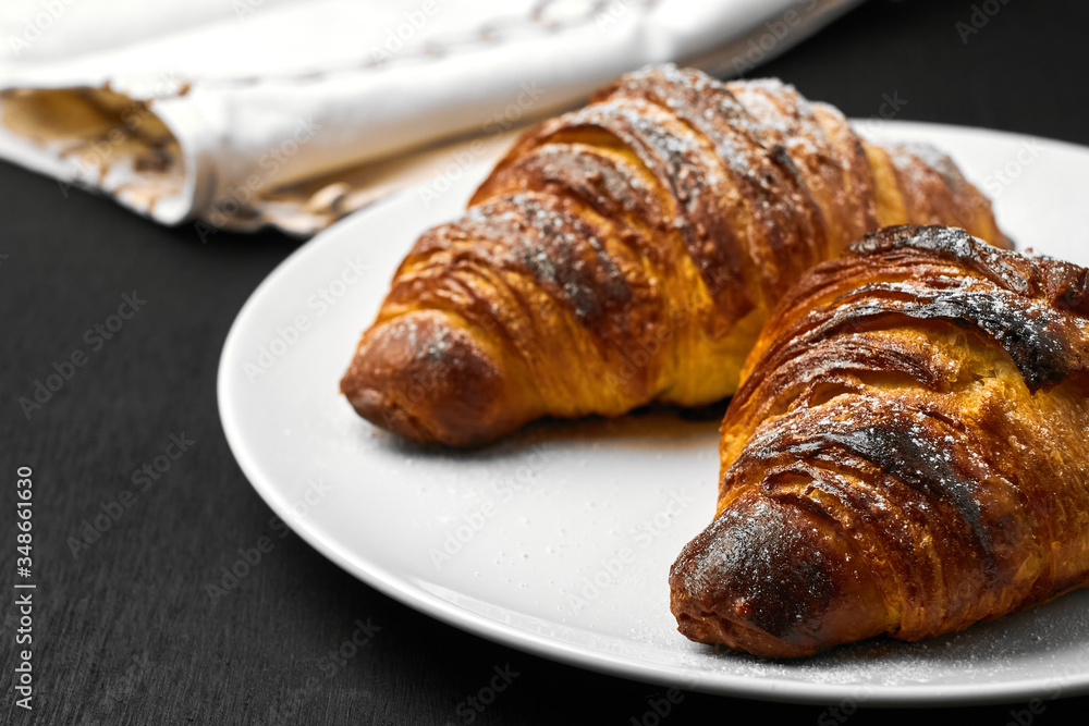 Freshly baked plain croissants on a white plate near serviette on a black wooden background. Homemade french pastry. Freshly baked plain croissants on a white plate near serviette on a black wooden background. Homemade french pastry.