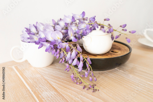 Beautiful spring flowers in teapot on wooden table  closeup. A traditional white ceramic teapot for hot green tea on a stand with lilac spring flowers.