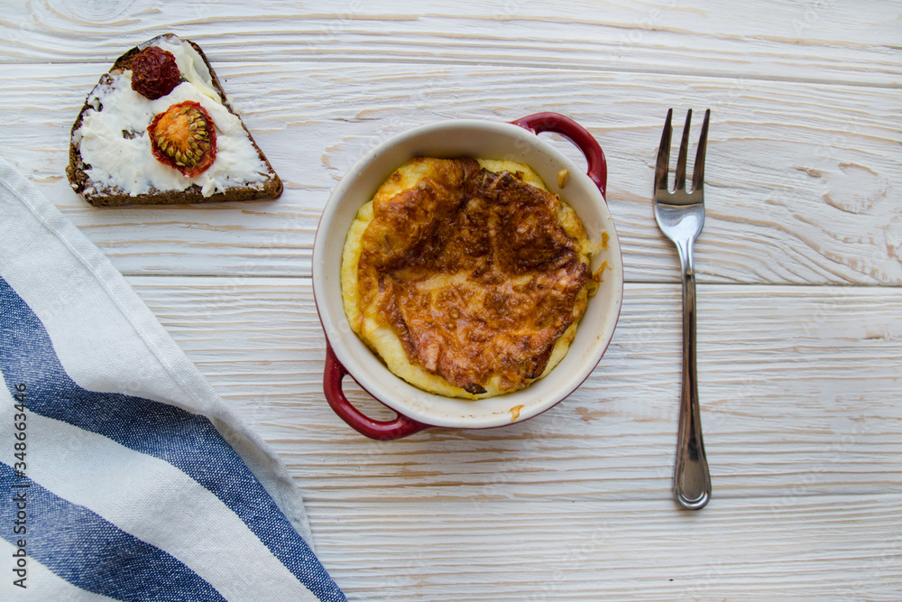 baked eggs with cheese in red ramekin served with tomato toast on white wooden background and white and blue striped napkin baked eggs with cheese in red ramekin served with tomato toast on white wooden background and white and blue striped napkin