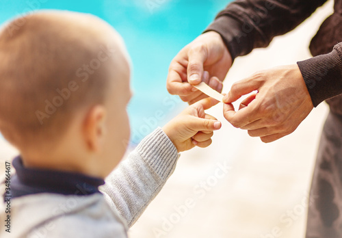 Dad putting a plater band-aid on his sons finger on white background, close-up, no face recognizable