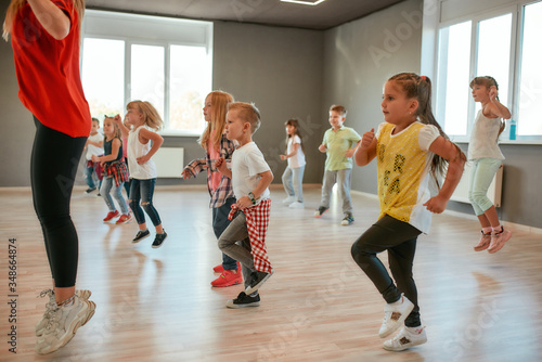 Fototapeta Naklejka Na Ścianę i Meble -  Studying modern dance. Group of little boys and girls dancing while having choreography class in the dance studio. Female dance teacher and children dancing
