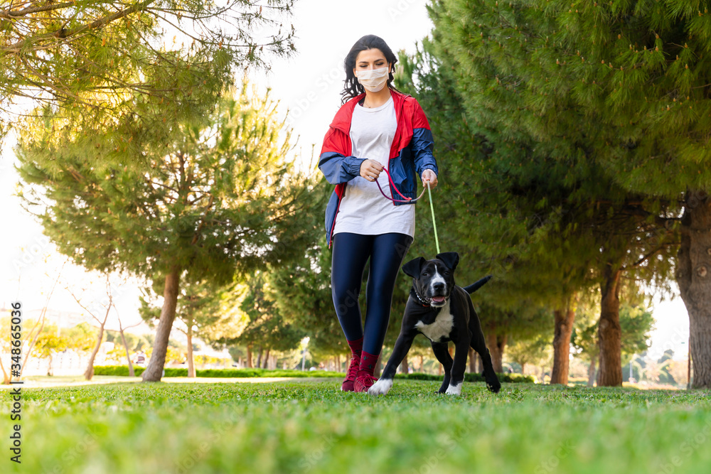 woman wearing a protective mask is walking alone with a dog outdoors because of the corona virus pandemic covid-19