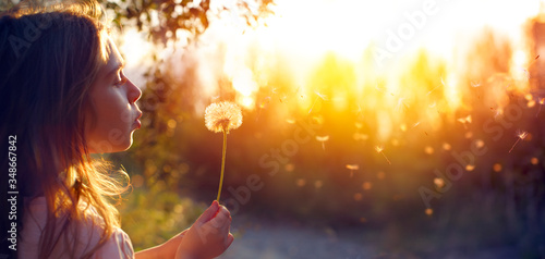 Valokuvatapetti Little Girl Blowing Dandelion Flower At Sunset - Defocused Background