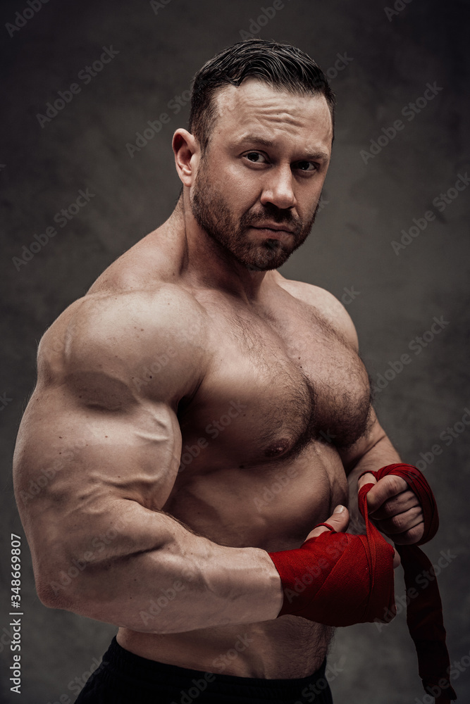 Sportive adult male wearing sportswear showing biceps, looking at the camera in a dark studio