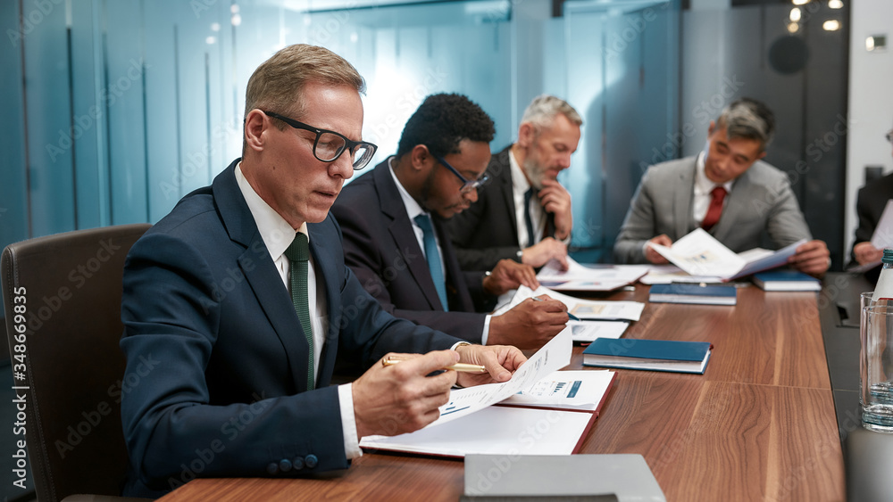 Concentrated business people in formal wear analyzing sales report while having a meeting in the office Concentrated business people in formal wear analyzing sales report while having a meeting in the office