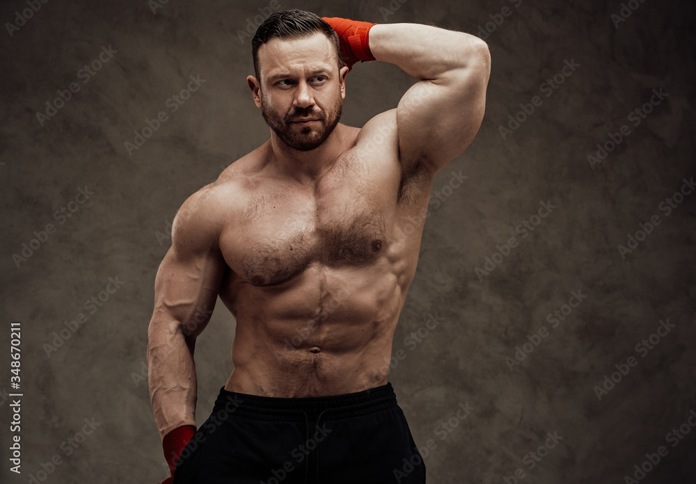 Shirtless adult male bodybuilder showing his huge muscles while posing in a dark studio