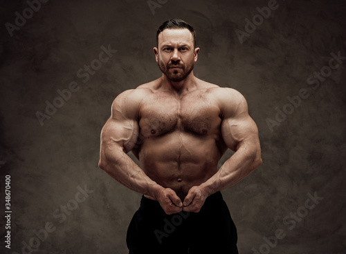 Shirtless adult male bodybuilder doing a muscle showing with a serious face in a studio © Fxquadro