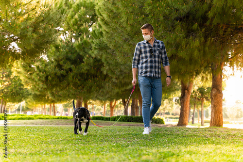 man wearing a protective mask is walking alone with a dog outdoors because of the corona virus pandemic covid-19