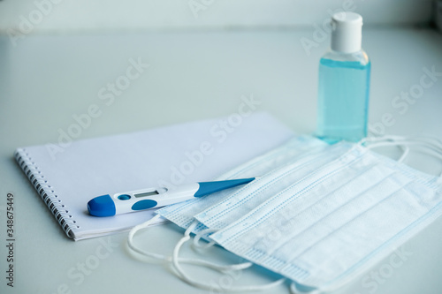 on a white table are a Notepad and protective equipment for the epidemic - medical masks, a thermometer and hand sanitizer
