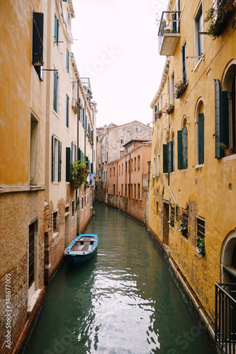 Boats moored at the walls of a building in a canal in Venice, Italy. Classic Venetian street views - wooden shutters, brick houses, bridges