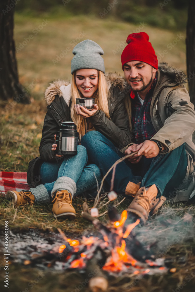 Traveler couple camping and roasting marshmallows over the fire in the forest after a hard day. Concept of trekking, adventure and seasonal vacation. Traveler couple camping and roasting marshmallows over the fire in the forest after a hard day. Concept of trekking, adventure and seasonal vacation.