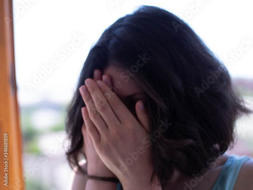 Young girl with short hair covers her face with hands.