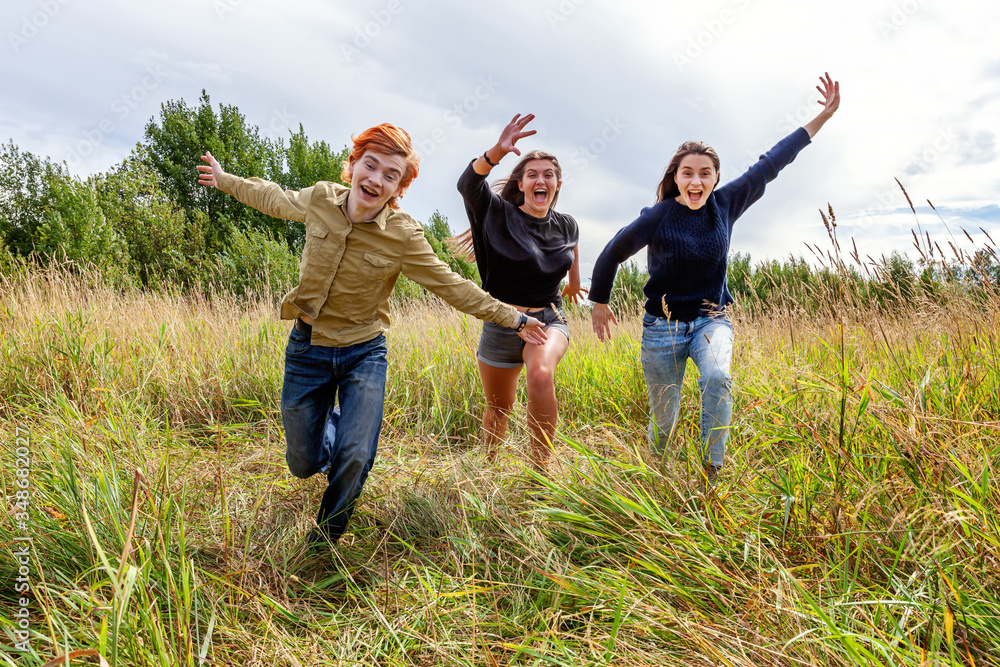 Summer holidays vacation happy people concept. Group of three friends boy and two girls running and having fun together outdoors. Picnic with friends on road trip in nature. Summer holidays vacation happy people concept. Group of three friends boy and two girls running and having fun together outdoors. Picnic with friends on road trip in nature.