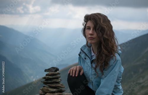 Adventurous girl siting on the edge of a cliff overlooking the beautiful . Beauty girl resting after jogging on the mountain road on the sunset with beautiful landscape view. The top of the mountain