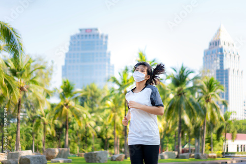 Asian young woman are jogging and exciseing outdoor in city park and wearing protective mask on face for stay in fit during Covid-19 pandemic in Bangkok, Thailand..