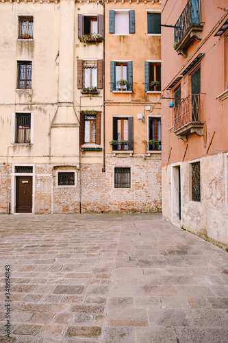 Close-ups of building facades in Venice, Italy. Ancient street, facades of peach and yellow buildings. Windows with wooden blue shutters. Stone paving tile
