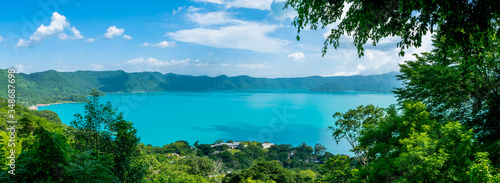 Panoramic view of the beautiful lake of Coatepeque in El Salvador, with a blue sky, in the season where its waters are turquoise and most of its mountains and vegetation are green.