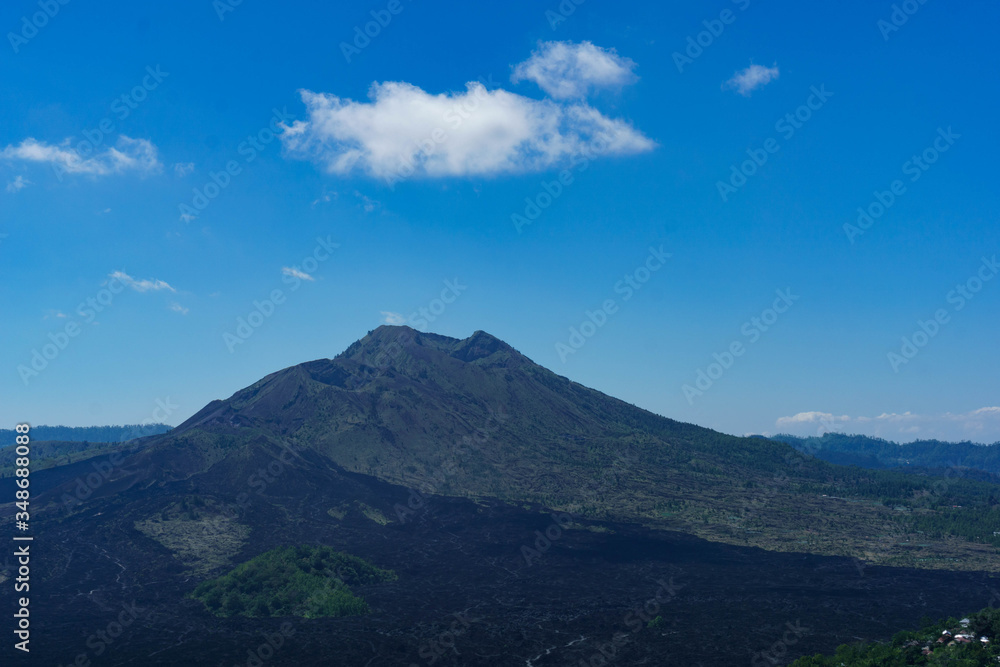 Slopes of a volcano mountain with black traces of lava with blue sky on background. Mount Batur (Gunung Batur) on the island of Bali, Indonesia. Slopes of a volcano mountain with black traces of lava with blue sky on background. Mount Batur (Gunung Batur) on the island of Bali, Indonesia.