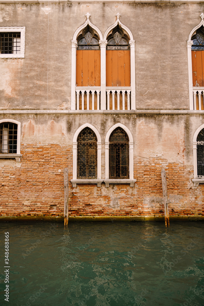 The facade of a corporatist apartment building in Venice, Italy. Buildings in waters of Venetian Canal. Typical Venetian windows with arches, columns and a sharp top, on the wall of a stone house. 
