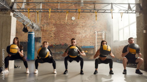 A fitness hub. Full length shot of sportive people in black sportswear using exercise ball while having workout at industrial gym. Group training, teamwork concept