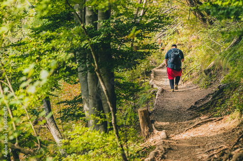 A seriously overweight person is descending down the mountain using hiking poles. Concept photo of a man loosing weight while hiking in the mountains. Sport, fitness and health.