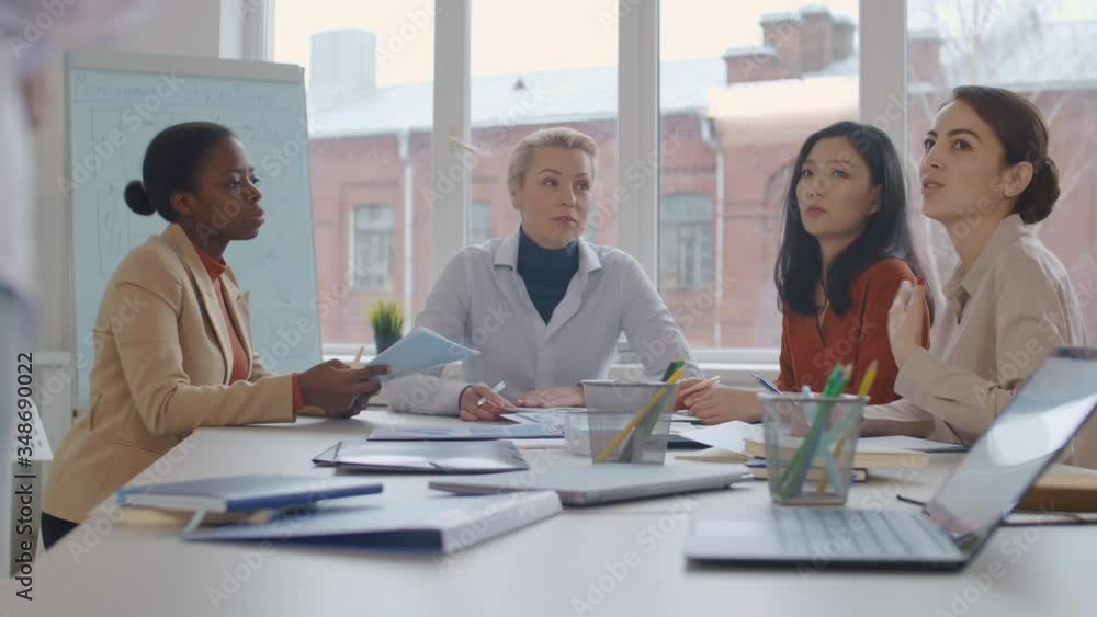 Rear view of unrecognizable leader talking to four multiethnic female colleagues sitting at desk in the office Rear view of unrecognizable leader talking to four multiethnic female colleagues sitting at desk in the office