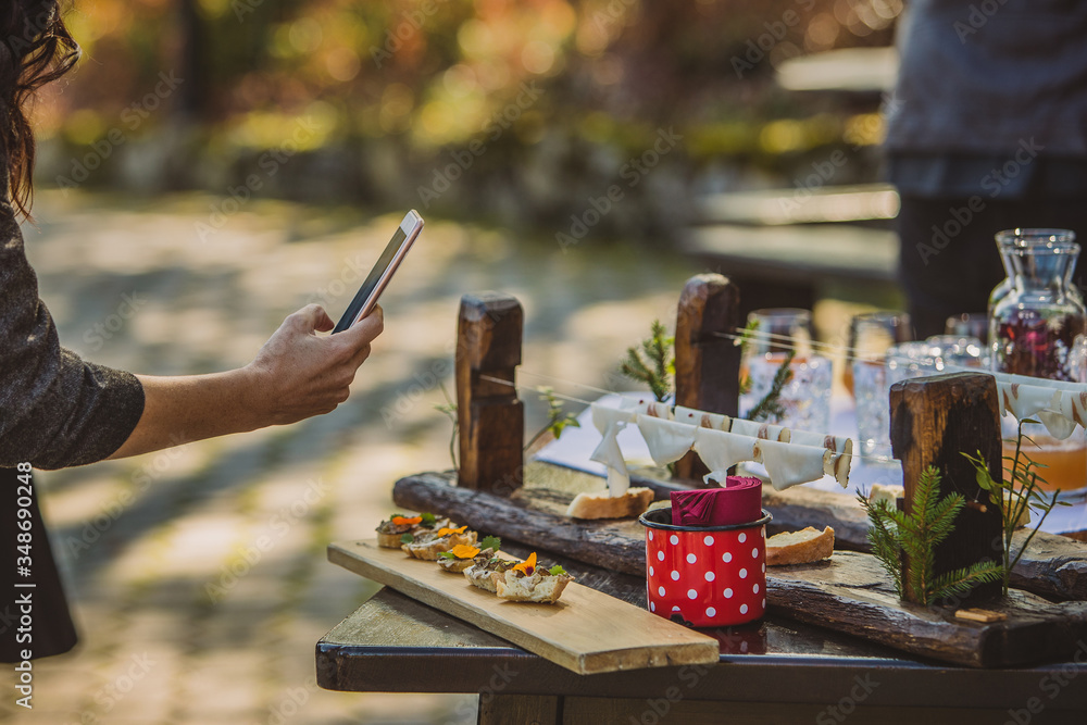 A person taking pictures of a fancy appetizer or small sandwiches on a gourmet event outdoors, served on a wooden board and fancy retro pots.