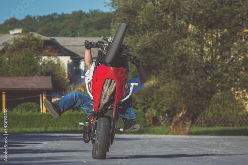 Motorcycle stunt man practicing on a home parking lot on a red and white motorcycle. Frontal view of a stuntman making a wheelie on a motorcycle. photo