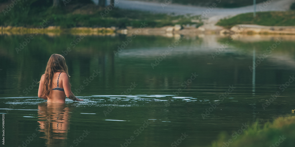 Fototapeta premium Young woman in a bikini bathing in a green cold lake.