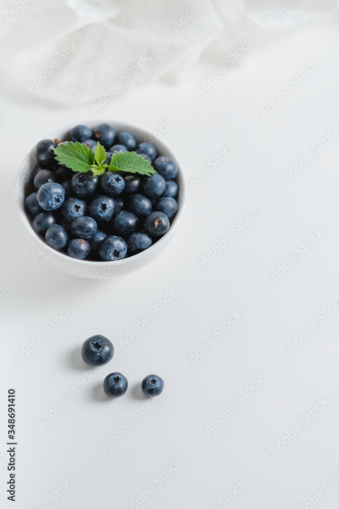 Fresh juicy blueberries with a sprig of mint in a white bowl with lace fabric on a white background. Fresh juicy blueberries with a sprig of mint in a white bowl with lace fabric on a white background.