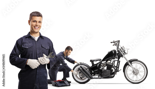 One mechanic holding a wrench and posing and other mechanic repairing a chopper motorbike