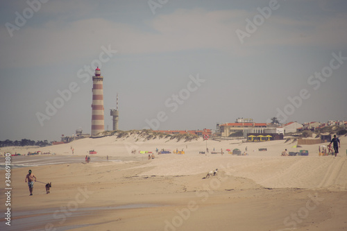 Sandy beach Praia da Barra in portugal on a sunny day with a big red and white lighthouse in the background.